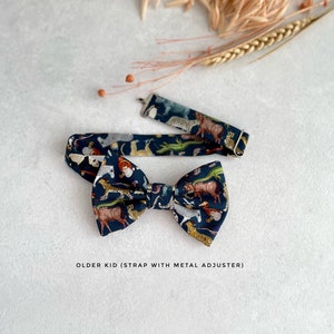 May include: A dark blue bow tie with a colorful animal print pattern. The bow tie has an adjustable strap with a metal buckle. "OLDER KID (STRAP WITH METAL ADJUSTER)" is printed below the bow tie.