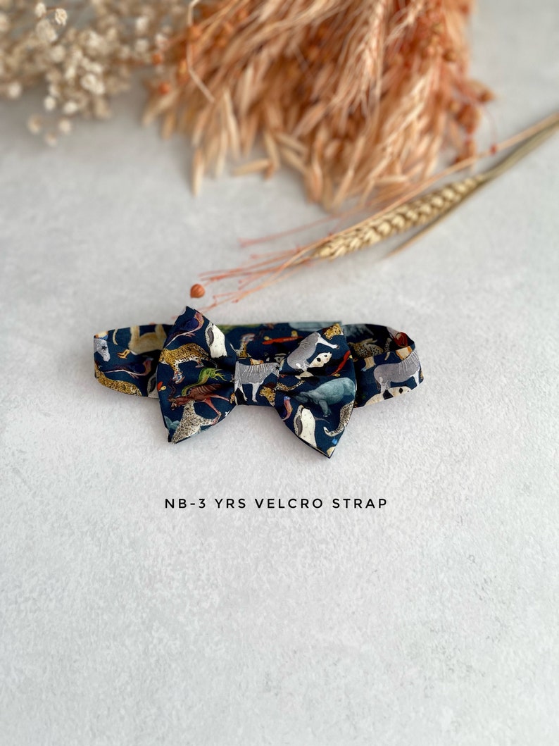 May include: A dark blue bow tie with a colorful animal print pattern. The bow tie has a velcro strap and is labeled "NB-3 YRS VELCRO STRAP".