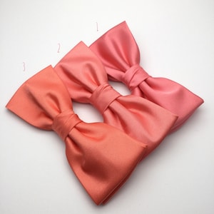 Puede incluir: Tres pajaritas de coral en diferentes tonos de coral. Las pajaritas están dispuestas en fila, con el tono de coral más oscuro a la izquierda y el tono de coral más claro a la derecha.