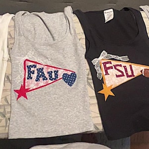 Op de afbeelding: Vier mouwloze tanktops in wit, grijs en zwart. Elke top heeft een wimpelontwerp met universiteitsinitialen en een ster. De wimpels zijn in verschillende kleuren, waaronder oranje, groen en blauw.