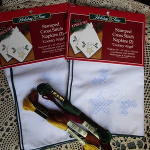 May include: Two sets of stamped cross stitch napkins with a "Country Angel" theme. Each napkin measures 14 x 14 inches and features a "Joy" design with a star and snowflake. Embroidery floss in various colors is included.