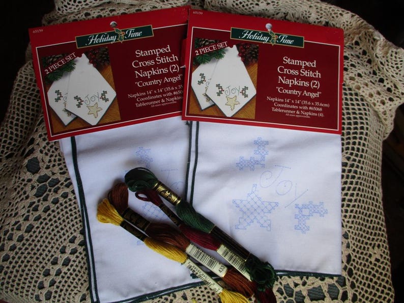 May include: Two sets of stamped cross stitch napkins with a "Country Angel" theme. Each napkin measures 14 x 14 inches and features a "Joy" design with a star and snowflake. Embroidery floss in various colors is included.
