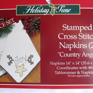 May include: A two-piece set of white cross-stitch napkins with the word "Joy" embroidered on them. The napkins are 14 x 14 inches and feature a "Country Angel" design. The package is red with the words "Holiday Time" at the top.