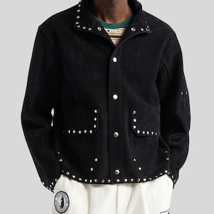 May include: Black corduroy jacket with silver stud detailing on the collar, pockets, and cuffs. The jacket has a button-up front and two front pockets. The model is wearing a striped shirt underneath. Part of a clothing collection.