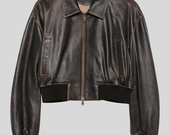 May include: A dark brown leather bomber jacket with a collared neckline and a zip-up front. The jacket has two front pockets and black ribbed cuffs and hem. The leather has a distressed, vintage look.