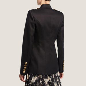 Puede incluir: Una chaqueta negra con botones dorados. La chaqueta tiene cierre de doble botonadura y cuello de muesca.