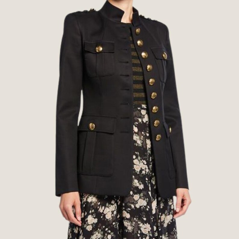 Puede incluir: Una chaqueta negra de estilo militar con botones dorados y cuello alto. La chaqueta tiene dos grandes bolsillos de solapa en la parte delantera y una silueta ajustada.