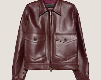 May include: A burgundy leather jacket with a collared neckline and a front zipper closure. The jacket features two front pockets with button closures. The interior lining is a contrasting color. The jacket is a classic outerwear piece.