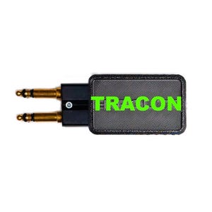 May include: A black electronic adapter featuring two gold-colored audio jacks on one side and a rectangular body with a textured surface. The word TRACON is printed in bright green capital letters across the center of the black rectangular housing.
