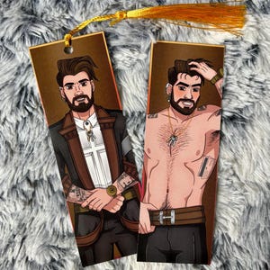 Könnte beinhalten: Zwei rechteckige Lesezeichen mit Illustrationen eines bärtigen Mannes. Eines zeigt den Mann im Anzug, das andere ohne Hemd. Beide haben eine goldene Quaste oben, zum Markieren von Seiten.