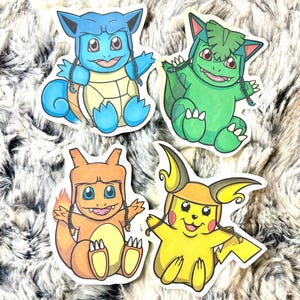 May include: Four colorful stickers featuring cartoon characters. The stickers include a blue turtle-like creature, a green dinosaur-like creature, an orange lizard-like creature, and a yellow mouse-like creature. Each character is wearing a hat and has a smiling expression.