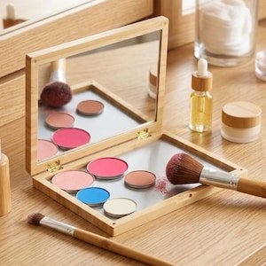 May include: A bamboo makeup palette with a mirror, holding eyeshadows in pink, blue, and neutral shades. Two makeup brushes and other beauty products are arranged on a wooden surface.