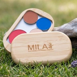 Puede incluir: Una paleta de maquillaje de bambú con cuatro sombras de ojos coloridas: rojo, marrón, azul y beige. La paleta está abierta, revelando un espejo y las sombras. La tapa cerrada muestra el texto "MILA SUSTAINABLE PACKAGING COMPANY".