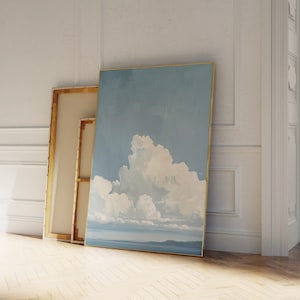Op de afbeelding: Twee ingelijste schilderijen leunen tegen een witte muur. Het schilderij aan de linkerkant is een blanco doek, terwijl het schilderij aan de rechterkant een blauwe lucht met een grote witte wolk toont.