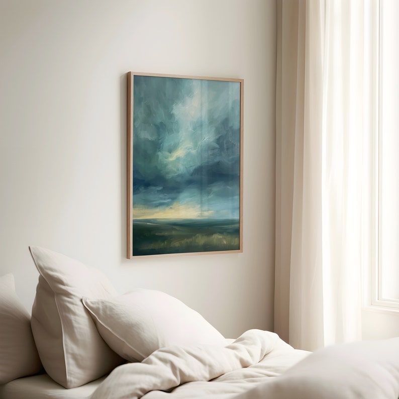 May include: An abstract landscape painting in a light wood frame. The artwork features a dramatic sky with shades of blue, green, and yellow, above a grassy field. The painting is displayed on a white wall above a bed with white linens.