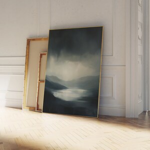 May include: A framed abstract landscape painting with a blue and gray color scheme. The painting depicts a misty scene with a lake and mountains in the distance.