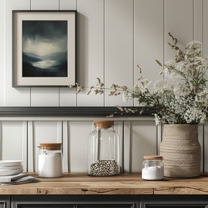 May include: Three glass jars with wooden lids on a wooden countertop. The jars are filled with white powder, white beans, and white powder. A vase with white flowers sits on the counter. The countertop is in front of a white paneled wall.