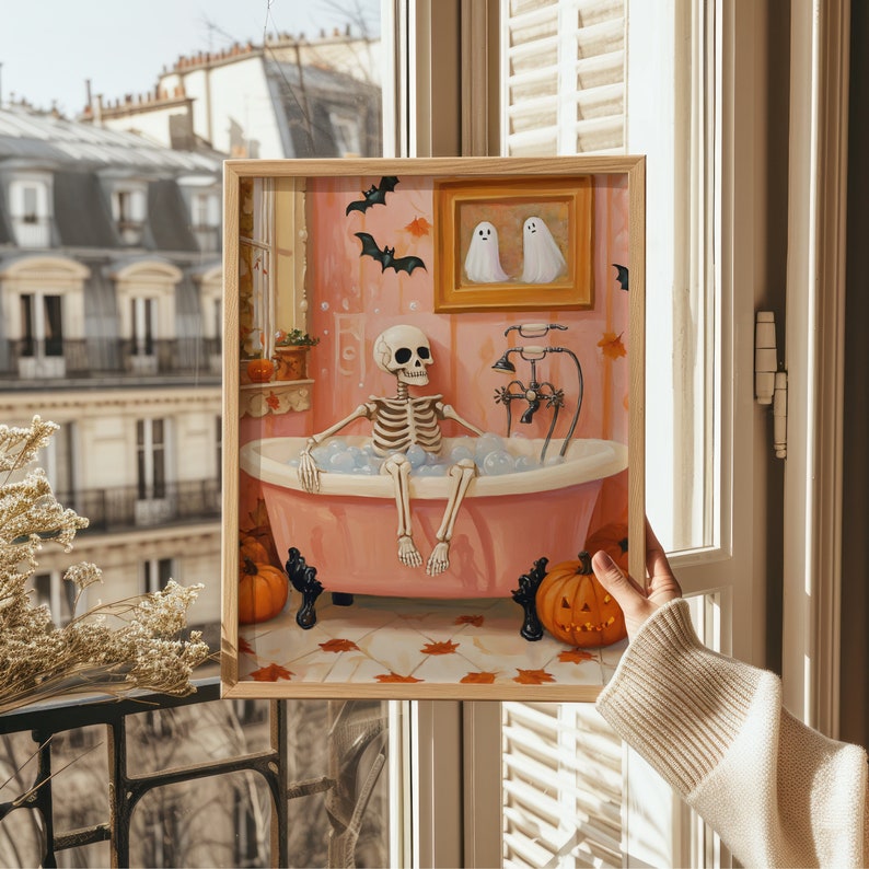 K&ouml;nnte beinhalten: Ein gerahmter Druck zeigt ein Skelett in einer rosa Badewanne mit Blasen, K&uuml;rbissen und Flederm&auml;usen. Ein Gem&auml;lde von zwei Geistern h&auml;ngt an der Wand. Das Kunstwerk hat ein Halloween-Thema.