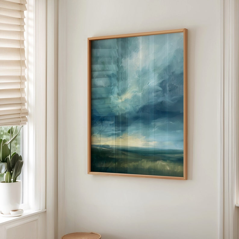May include: An abstract landscape painting in a light wood frame. The artwork features a blend of blues, greens, and yellows, depicting a cloudy sky over a field. The painting is displayed on a white wall near a window with blinds.