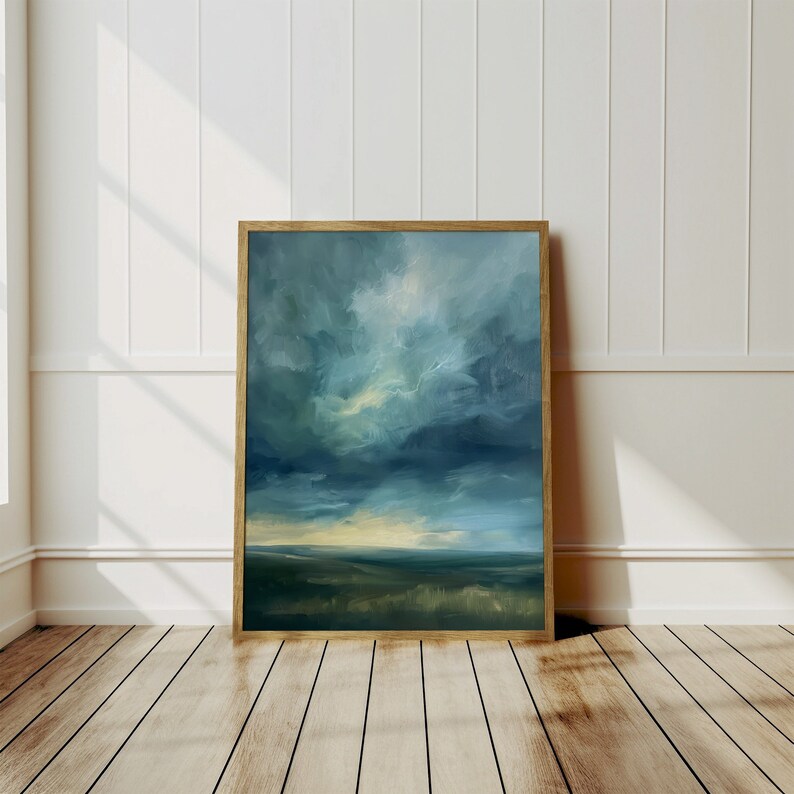 May include: An abstract landscape painting in a wooden frame. The artwork features a dramatic sky with shades of blue and white, and a dark green and yellow landscape. The painting is displayed against a white wall and wooden floor.
