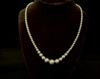 May include: A silver necklace with round beads, displayed on a black velvet stand.
