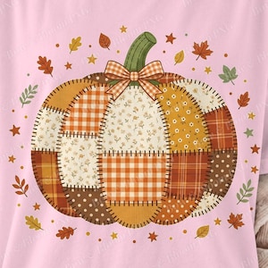 May include: A light pink t-shirt featuring a large central pumpkin graphic composed of various patchwork patterns including orange gingham, floral prints, and brown polka dots. The pumpkin is topped with a green stem and an orange plaid bow.