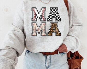May include: A light grey crewneck sweatshirt featuring the word MAMA in large block letters. Each letter has a unique pattern: the first M has red baseball stitching, the A has a black and white checkerboard, the second M has pink bows, and the final A has a brown leopard print.