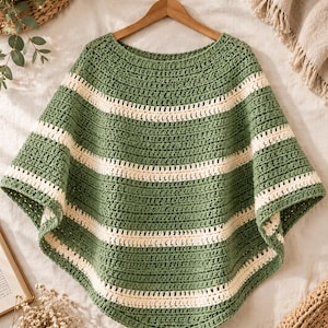 May include: A crochet poncho featuring a wide boat neckline and a repeating horizontal striped pattern. The garment is constructed with alternating bands of sage green and cream-colored yarn, creating a textured, layered appearance throughout.