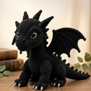 Può includere: Un peluche a forma di drago lavorato all'uncinetto in nero, con grandi occhi verde chiaro, orecchie a punta e piccole corna sulla testa. La creatura presenta ali dettagliate, una lunga coda e piccoli artigli argentati sui piedi in filato.