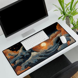 Puede incluir: Una alfombrilla de escritorio rectangular grande con un diseño de olas y puesta de sol de estilo japonés en tonos azules, naranjas y blancos. Un teclado y un ratón blancos están sobre la alfombrilla. Un monitor de ordenador está en el fondo.