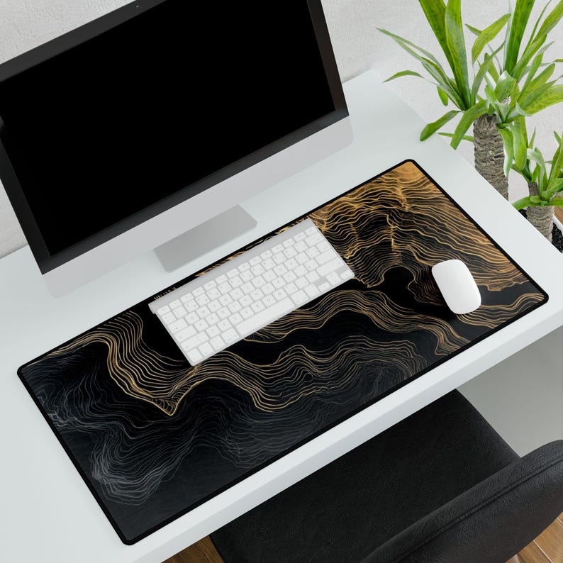 A large black and gold desk mat with a unique wavy lined design. A white keyboard and mouse sit on the mat, next to a computer monitor. The mat is rectangular and covers a large portion of the desk.