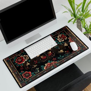 May include: A rectangular desk mat with a dark brown background featuring a floral and butterfly design in red, green, and yellow. The mat has a decorative border and is shown with a white keyboard and mouse.