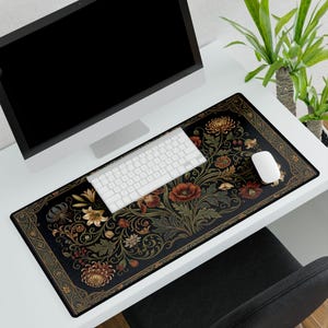 May include: A black rectangular desk mat with a floral design featuring red, gold, and green flowers and foliage. The mat has a decorative border and is shown with a white keyboard and mouse.