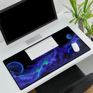 May include: A black rectangular desk mat with a space-themed design featuring planets and nebula clouds in shades of blue and green. A white keyboard and mouse are on the mat, with a computer monitor in the background.