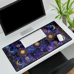 May include: A rectangular desk mat featuring a celestial design with gold suns, moons, and stars against a deep blue and purple galaxy background. The mat is placed under a computer, keyboard, and mouse.