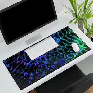 May include: A black desk mat with a vibrant, abstract design in shades of blue, green, and purple. A white keyboard and mouse sit on the mat, with a computer monitor in the background. The mat is rectangular and covers a large portion of the desk.