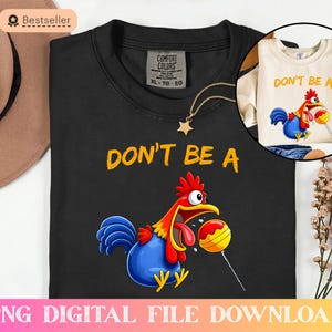 Könnte beinhalten: Schwarzes T-Shirt mit dem Text "DON'T BE A" und einem Cartoon-Hahn, der einen Lolli hält. Ein kleineres Bild zeigt ein cremefarbenes Langarmshirt mit dem gleichen Design. Eine goldene Stern-Anhänger-Halskette ist ebenfalls vorhanden.