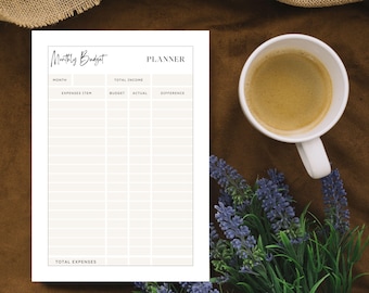 May include: A monthly budget planner with a minimalist design. The white paper has sections for income, expenses, and budget tracking. A white mug of coffee and lavender sprigs are next to the planner on a brown surface.