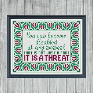 Könnte beinhalten: Gerahmtes Kreuzstich-Kunstwerk mit schwarzem Rahmen. Der Text lautet: „Man kann jederzeit behindert werden. DAS IST NICHT NUR EINE TATSACHE, ES IST EINE BEDROHUNG.“ Das Design hat einen grünen und weinroten Blumenrand.