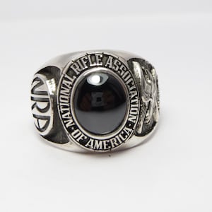 May include: A silver ring with a black stone and the inscription "National Rifle Association of America".