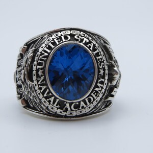 May include: A silver ring with a blue stone and the inscription "UNITED STATES NAVAL ACADEMY".