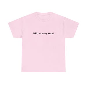 May include: A light pink t-shirt with the text "Will you be my koan?" in black, centered on the front. The shirt has a crew neck and short sleeves, made of a soft, casual fabric.