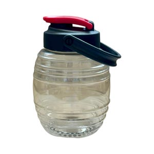 May include: A clear plastic water bottle with a black lid and a red handle. The bottle has a barrel shape and is designed for carrying water.