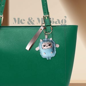 May include: A green tote bag with a light blue and white sheep keychain attached. The keychain has a small, angry-looking face.
