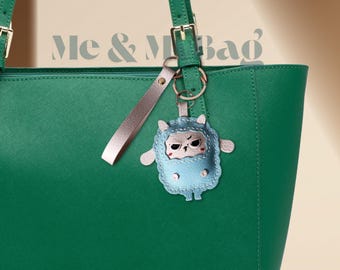 May include: A green tote bag with a light blue and white sheep keychain attached. The keychain has a small, angry-looking face.