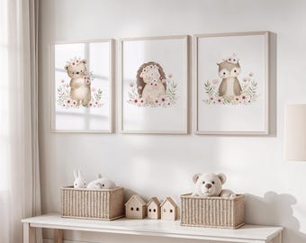 Könnte beinhalten: Drei gerahmte Aquarelldrucke mit Waldtieren: einem Bären, einem Igel und einer Eule, jeweils mit Blumenkränzen geschmückt und von Blumen umgeben. Darunter befinden sich zwei Weidenkörbe mit Stofftieren und Miniatur-Holzhäuser, die das Regal schmücken.