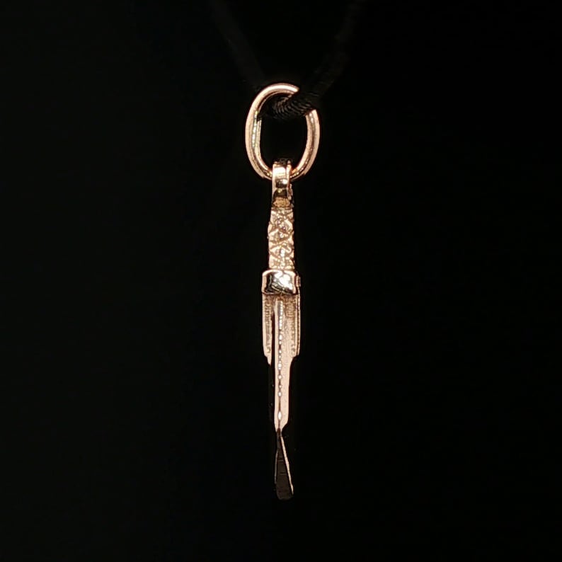 Antique bronze Cloud Strife sword charm from FFVII Final Fantasy gamer jewelry. Small FF7 Buster Sword charm in antique bronze Final Fantasy Cloud Strife pendant. Close up of small Buster Sword pendant in bronze FF7 inspired cosplay accessory. Mini Final Fantasy sword charm in bronze Cloud Strife cosplay gift