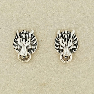 Op de afbeelding: Een paar zilverkleurige oorknopjes met een gedetailleerd, gestileerd wolvenkopontwerp. Elke oorbel toont een naar voren gerichte wolf met puntige oren en een textuurrijke manen, met een kleine ring die aan de snuit van de wolf hangt.