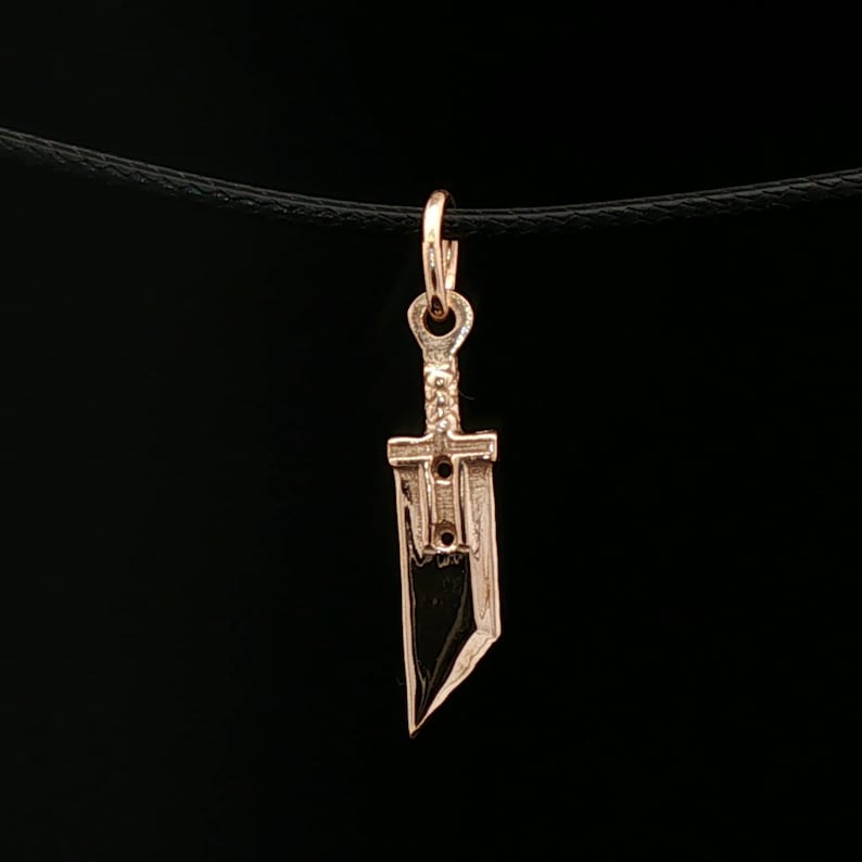 Antique bronze Cloud Strife sword charm from FFVII Final Fantasy gamer jewelry. Small FF7 Buster Sword charm in antique bronze Final Fantasy Cloud Strife pendant. Close up of small Buster Sword pendant in bronze FF7 inspired cosplay accessory. Mini Final Fantasy sword charm in bronze Cloud Strife cosplay gift