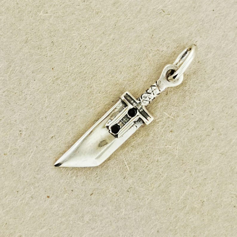 Small FF7 Buster Sword charm in sterling silver Final Fantasy Cloud Strife pendant. Close up of small Buster Sword pendant in silver FF7 inspired cosplay accessory. Mini Final Fantasy sword charm in sterling silver Cloud Strife cosplay gift.